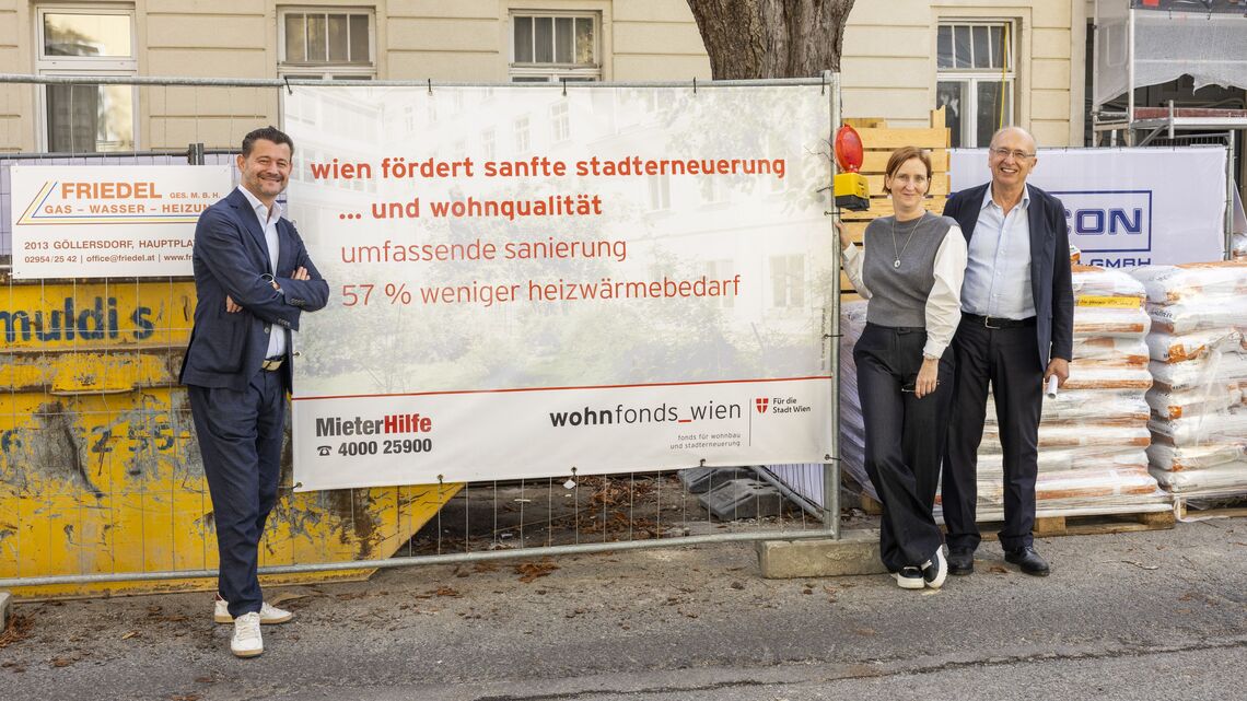 Drei Personen stehen vor einem Bauzaun mit einem Banner, das Informationen zur Stadtentwicklung und Wohnqualität in Wien zeigt