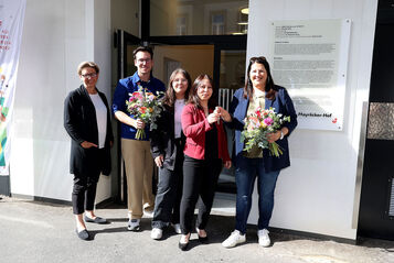 Wiener Wohnen Direktorin Karin Ramser, Bezirksvorsteher Michael Luxenberger und Vizebürgermeisterin und Wohnbaustadträtin Kathrin Gaál mit frisch eingezogenen Bewohnerinnen stehen vor dem Eingang des Gemeindebau NEU in der Schönbrunnerstraße. Kathrin Gaál überreicht der neuen Mieterin symbolisch ihren Wohnungsschlüssel. Sie hält dabei auch einen bunten Blumenstrauß in der Hand, ebenso wie der Bezirksvorsteher von Margareten