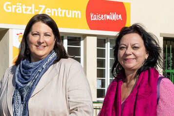 Viezbürgermeisterin Gall steht mit wohnpartner-Bereichsleiterin Claudia Huemer vor einem Gebäude. Über dem Eingangsportal ist der Schriftzug Grätzl-Zentrum Kaisermühlen zu lesen..