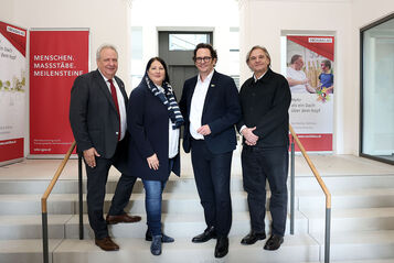 Drei Männer und eine Frau stehen auf Stufen in einem alten aber frischrenovierten Stiegenhaus.