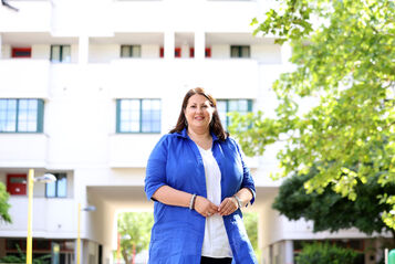 Vizebürgermeisterin Kathrin Gaál steht vor einem neuen Gebäude, sie trägt ihre die brauen Haare offen und ist mit einer blauen langen Bluse über weißem T-Shirt bekleidet.