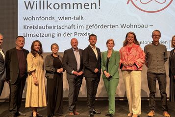 Gruppe von zehn Personen steht vor einer Präsentationswand mit dem Text 'Willkommen! wohnfonds_wien-talk Kreislaufwirtschaft im geförderten Wohnbau – Umsetzung in der Praxis'