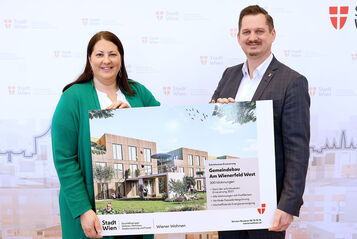 Eine Frau und ein Mann halten ein Schild mit der Visualisierung des neuen Gemeindebaus NEU in der Siedlung Wienerfeld West, erkennbar an der Beschriftung des Schildes. Sie lächeln in die Kamera.