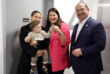 Vizebürgermeisterin und Wohnbaustadträtin Kathrin Gaál und Bezirksvorsteher Alexander Nikolai in der neuen Wohnhausanlage übergeben einer Frau mit Baby am Arm die Schlüssel zu ihrer neuen Wohnung.