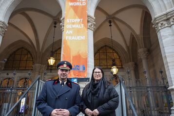 Ein hoher Polizeibeamter in Uniform mit Mantel und die Vizebürgermeisterin im Wintermantel posieren vor der am Wiener Rathaus gehissten orangen Flagge mit der Aufschrift "Orange the World" und "Stoppt Gewalt an Frauen!"